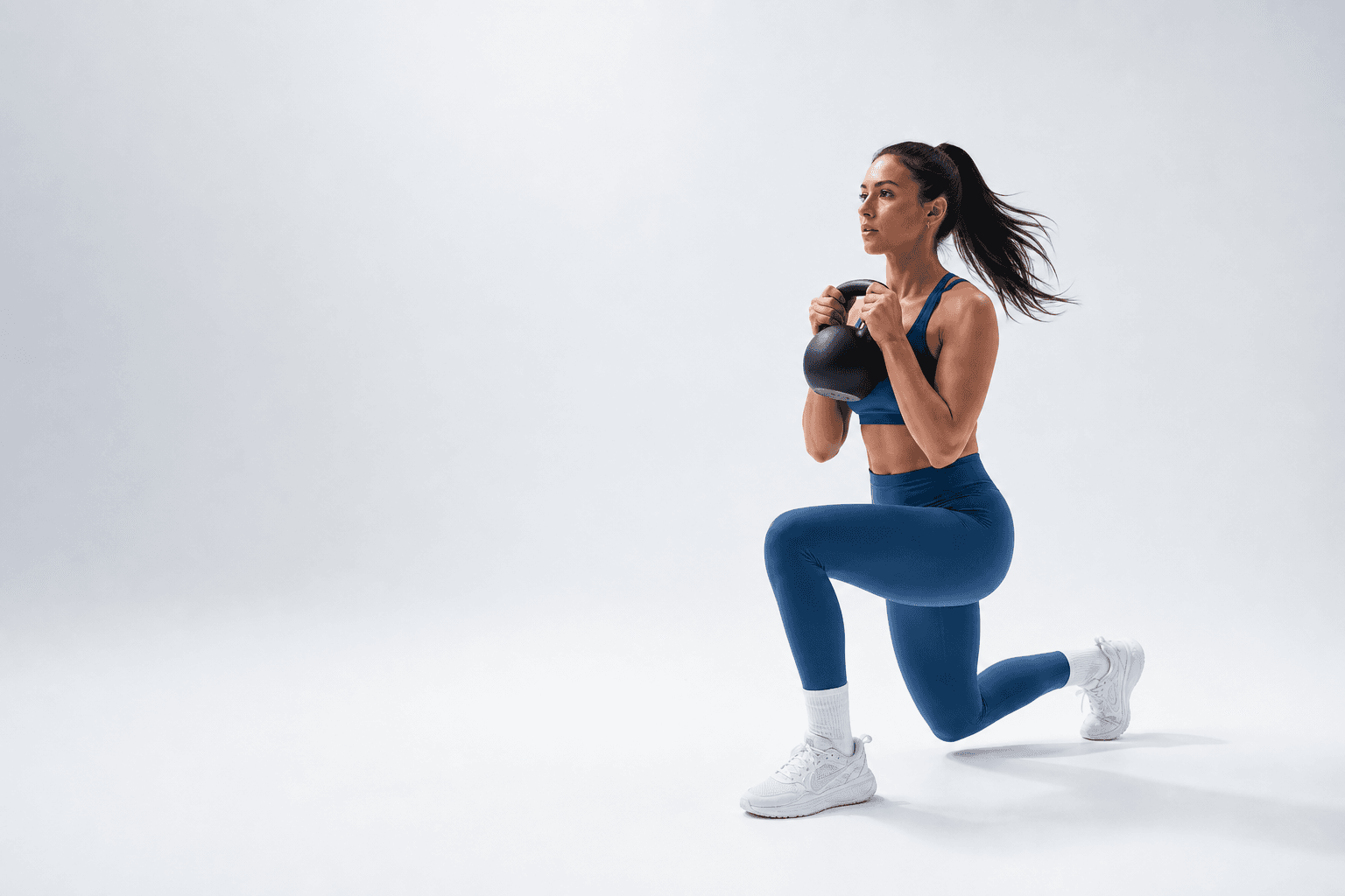 An athlete in blue training with a kettlebell in a bright white studio